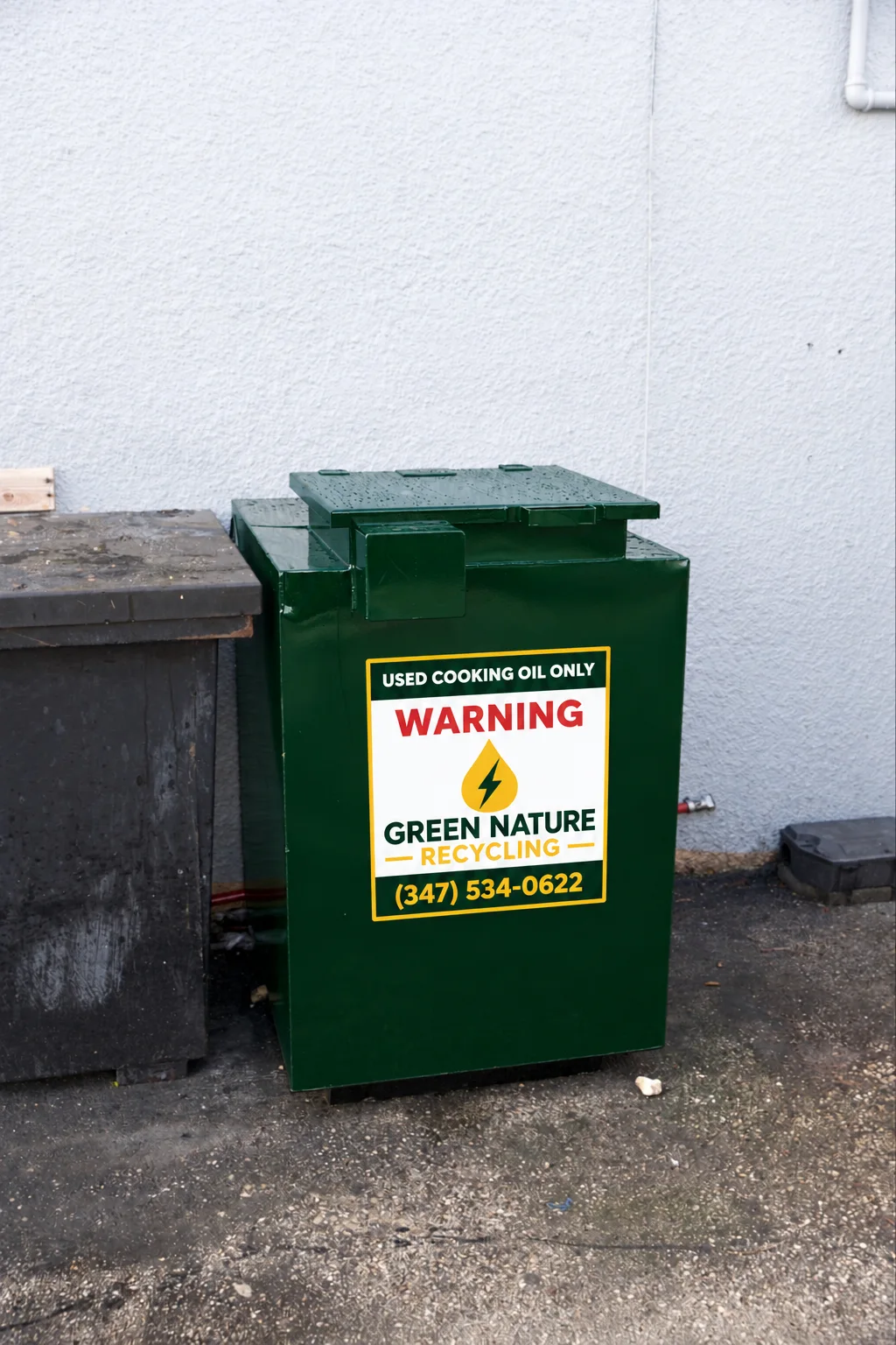 Green used cooking oil container beside a worn metal bin